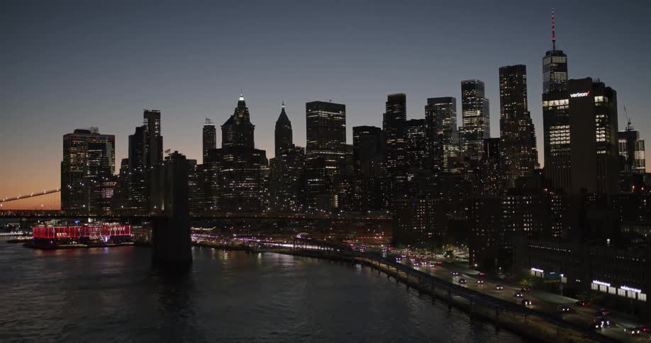 Headlights moving in blurred lines along the shoreline road beside the bay with the city skyline silhouetted in against the sky as it becomes darkerdusk