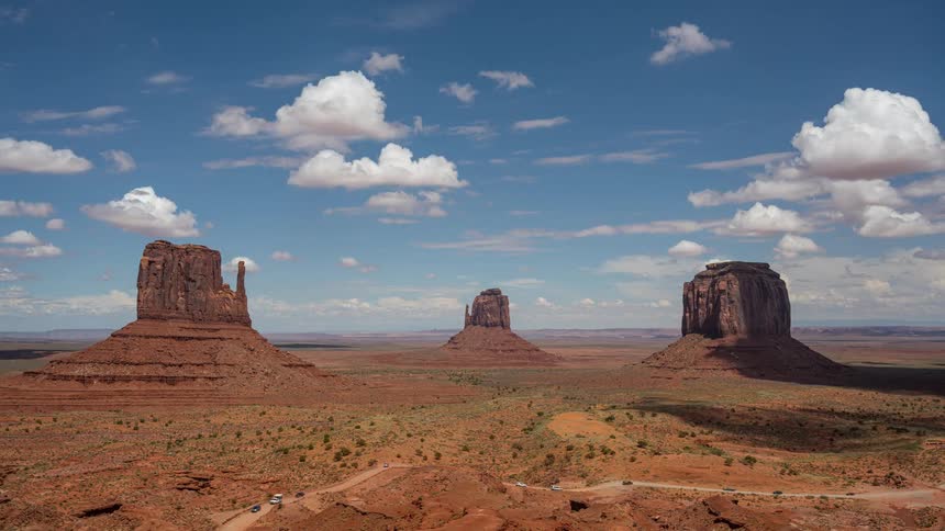 Cumulus clouds move over buttes in the desert as traffic moves on the roads