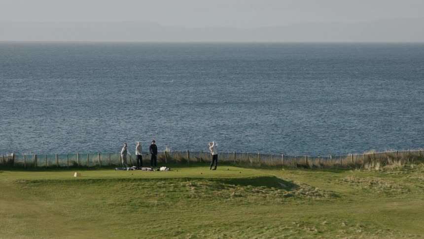 A group of four people are playing golf on a course by the ocean beach on a sunny day