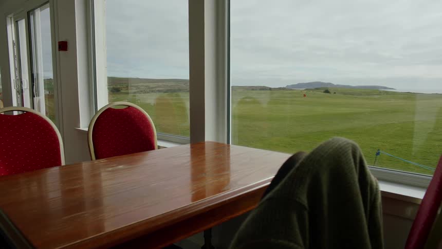 A table and chairs are positioned near a window overlooking a grassy plain