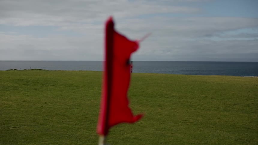 A blowing red flag planted by the sea side at midday