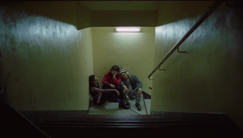 Three females sit by the stairs with their backs against the wall