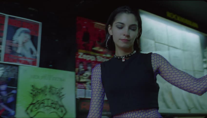 Woman walks down staircase passing band posters and other club patrons