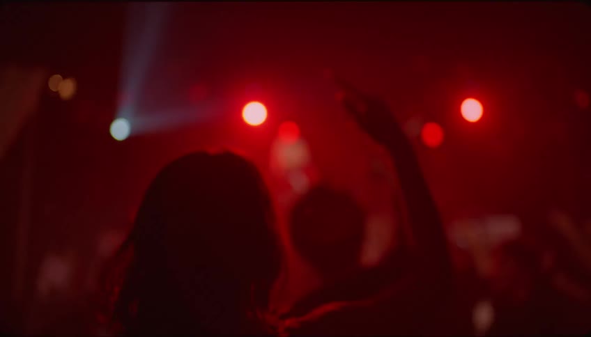 Lady walks into a club to dance with others while someone sings on stage at night