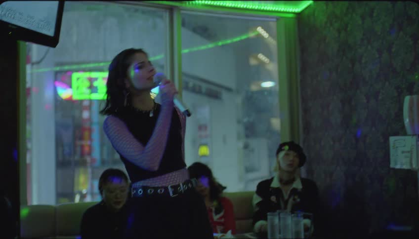 Woman singing at karaoke with her friends sitting in a pub watching
