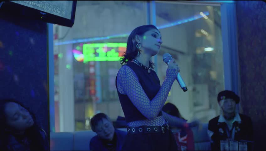Young woman singing karaoke at night in a room illuminated by colorful led lights