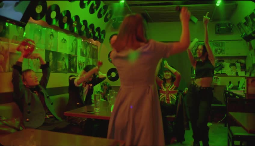 Two young women dancing energetically in a pub while her friends clap from the table