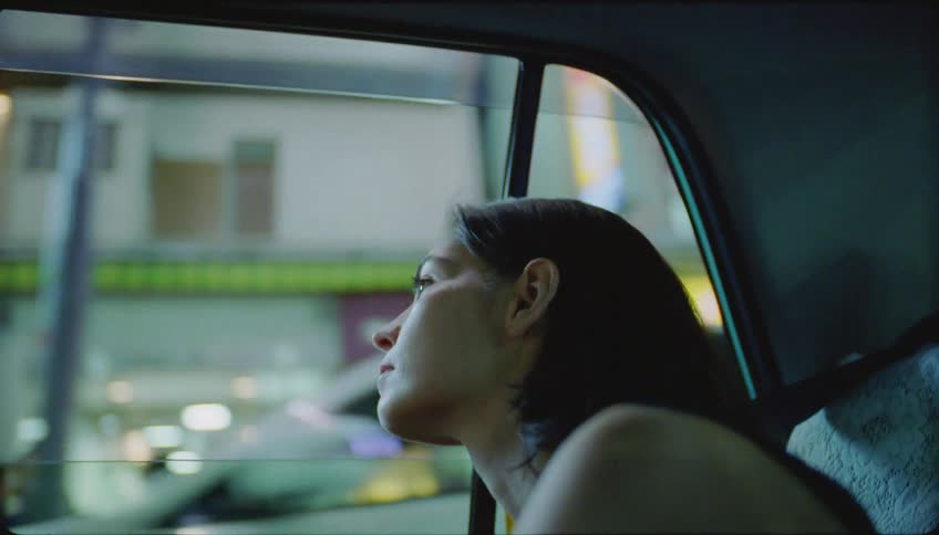 A woman is sitting in a car and looking for jane in a city with several lights