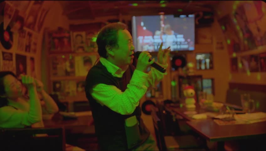 People in a pub with an elderly person singing at a karaoke