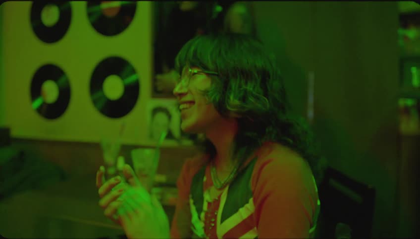 Energetic women dancing and clapping while seated at a table in a dimly lit pub with green lighting enjoying music