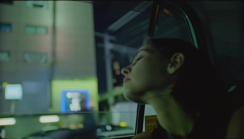 Woman sitting in the back seat of the car gazing at the city at night through the window
