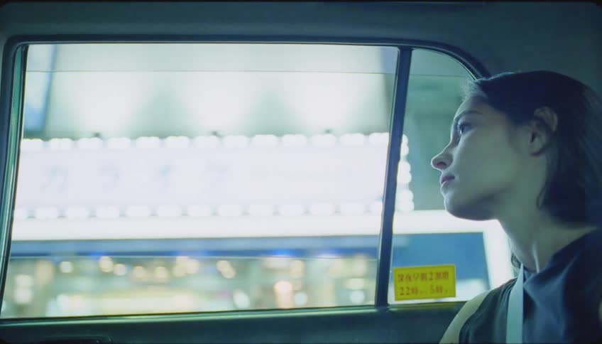 A young woman sits in the back of a vehicle driving through a metropolitan area