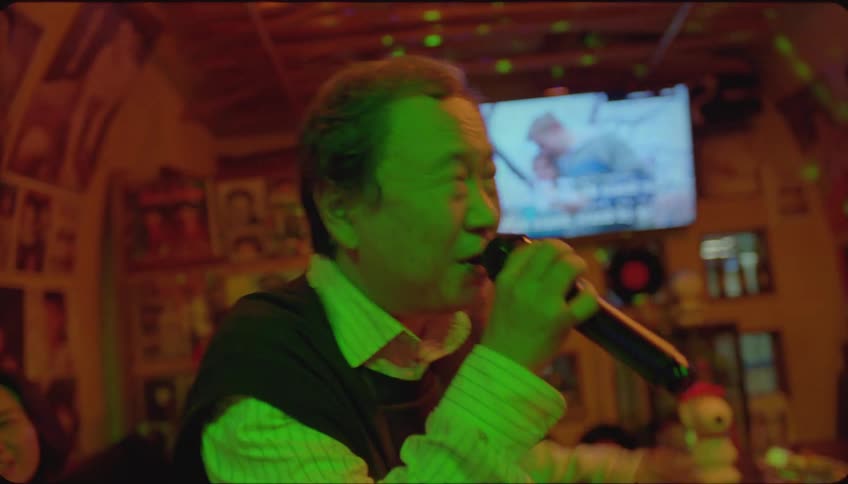 Man singing karaoke in a pub with friends and family cheering for him