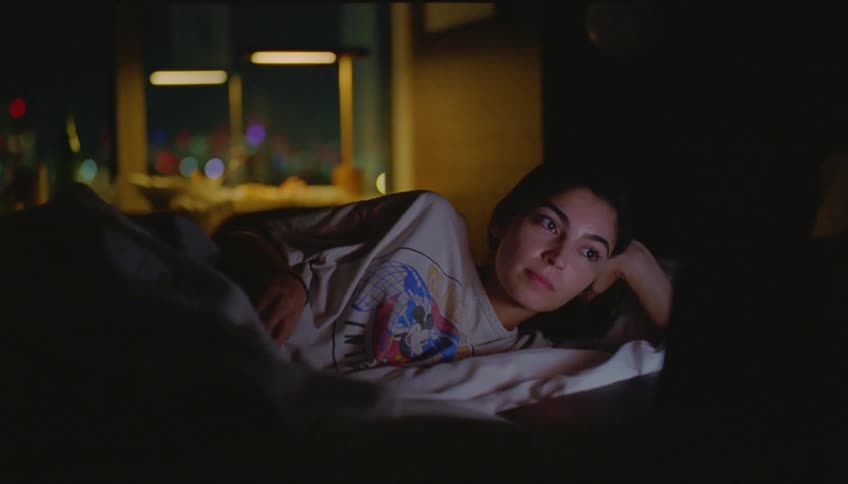 Young woman lying in bed watching a movie on her laptop