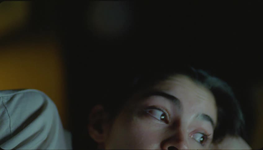 Close up of woman lying down and watching television in a dark room