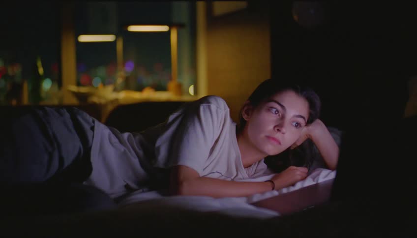 Woman lying on the bed watching something on the laptop screen at night