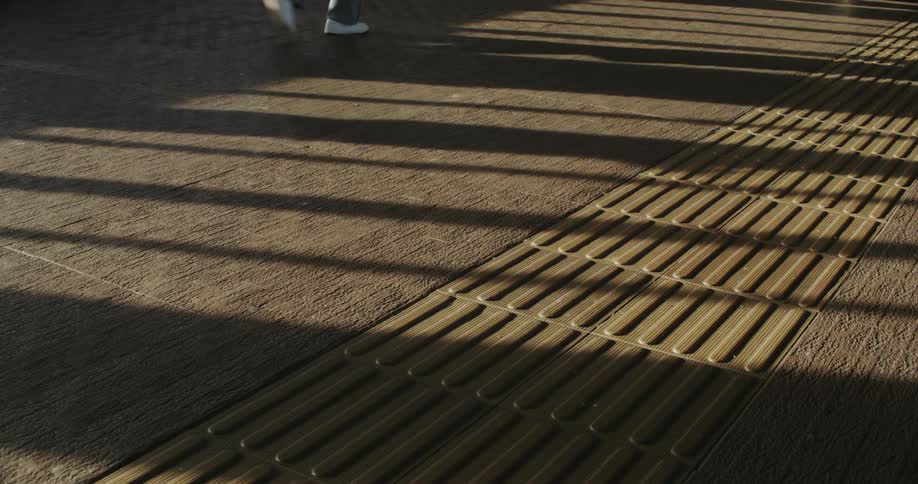 Walkway with a path for visually impaired individuals with shadows of people passing by