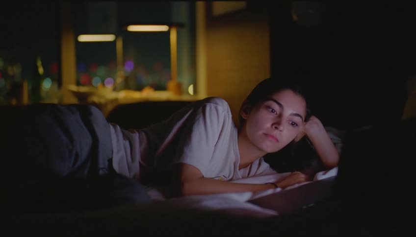 Woman lying on the sofa in the living room at night using her laptop and then closing it