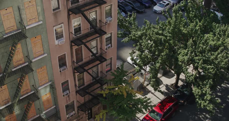 Pedestrians walk along sidewalk bordering apartment parking lot