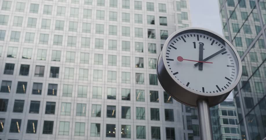 View of a clock in front of an entirely mirrored building in a metropolis