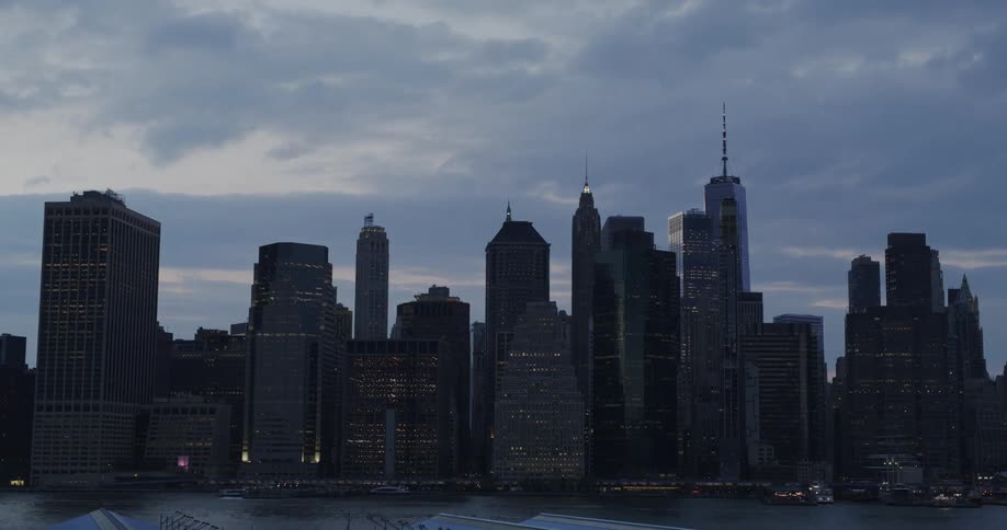 Clouds moving quickly across the sky above the city skyline while boats blur across the waterfront at dusk