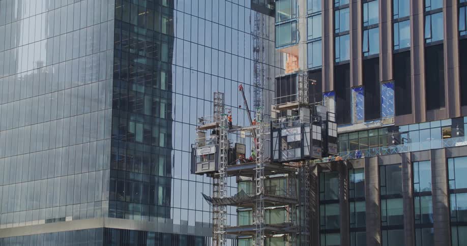 Construction works rest on a platform several stories up a glass building