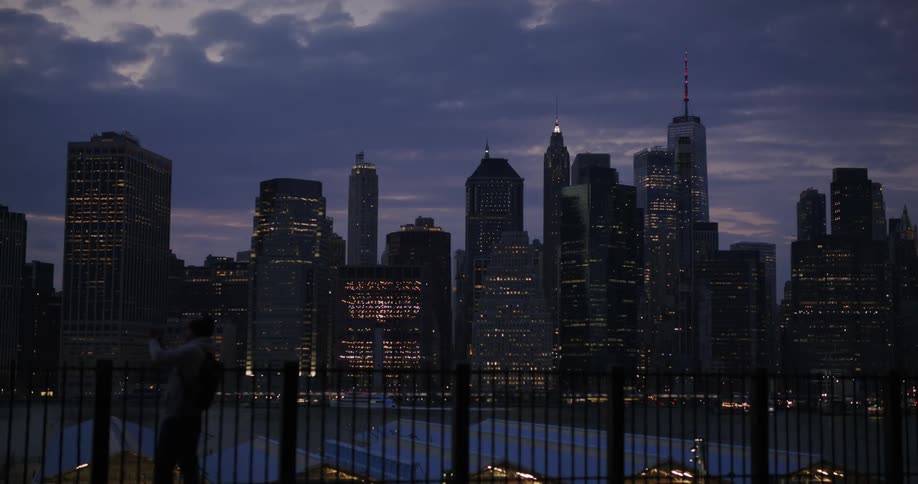 A cityscape illuminated at dusk with lights flickering as night begins to fall