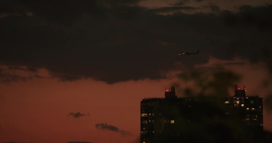 View of buildings with an airplane landing against a reddish sky