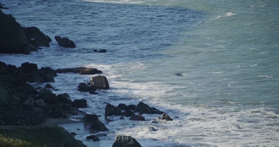 Waves roll into shore and splash against rocks along the coast