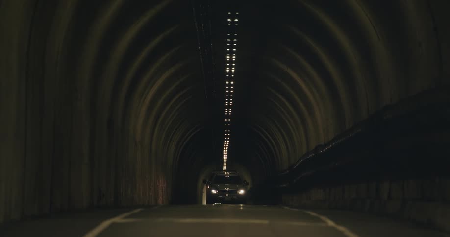 Automobiles travel on a road through a tunnel with lights on the ceiling