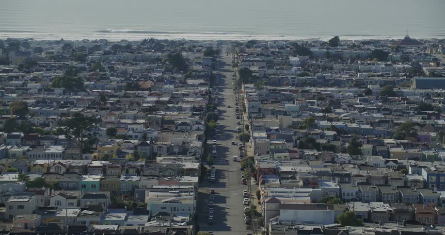 Vehicles move along large street through residential neighborhood bordering coast