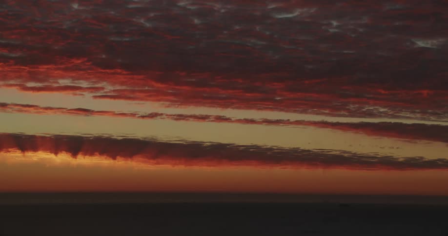 Clouds float over the water as they reflect the sunlight in an orange sky