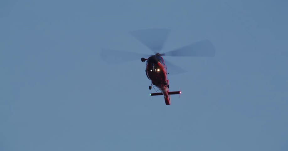 A red helicopter flies in a clear blue sky