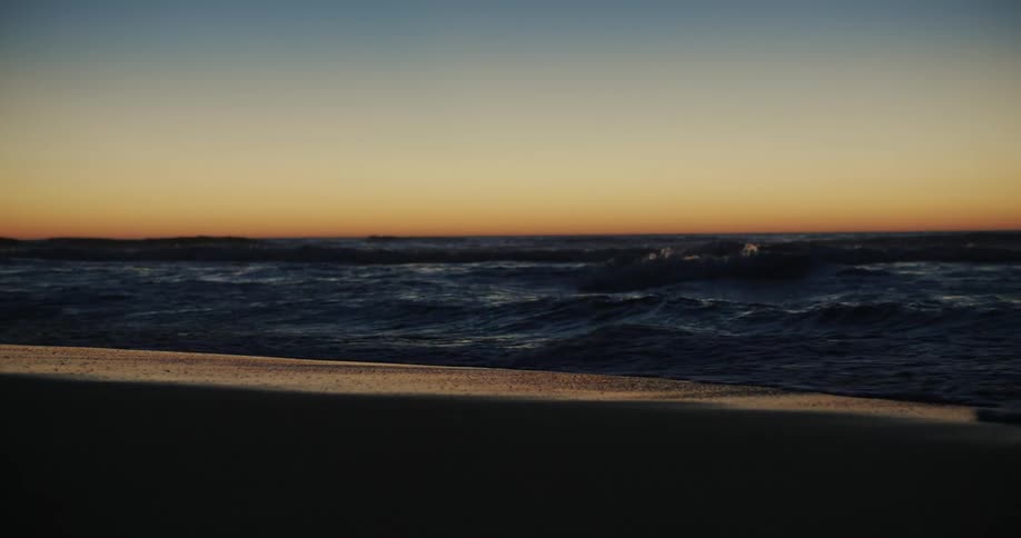 Ocean waves breaking against the sandy beach at dusk