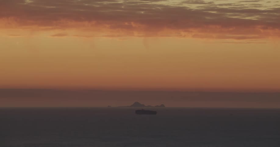 A boat sails under colorful clouds over the water at sunset with mountains in the distance
