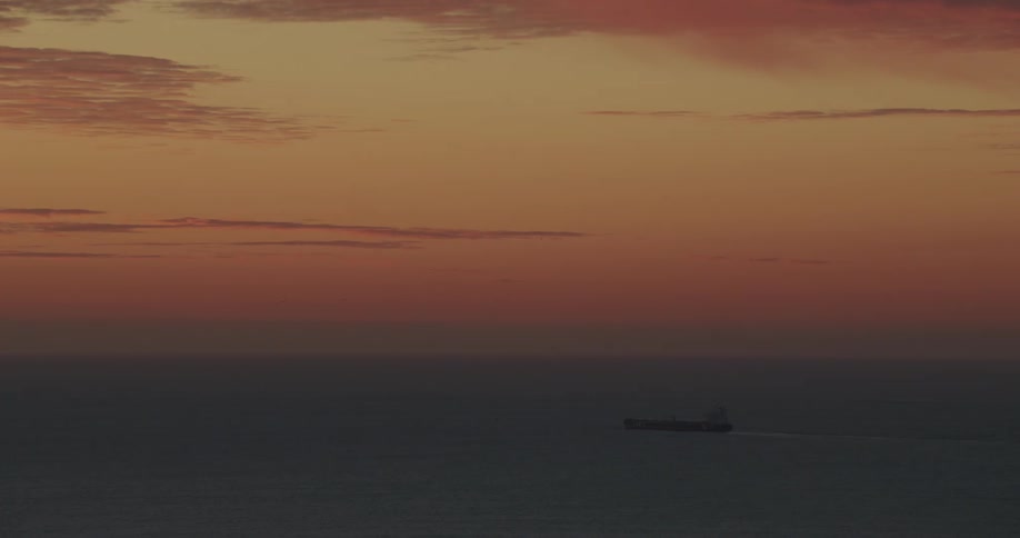 A ship sails under colorful clouds over the water at sunset