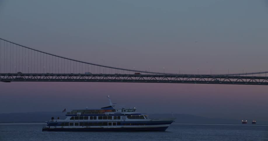 A ship sailing in the sea under the suspension bridge during dusk