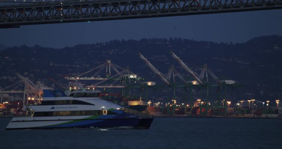 A yacht sailing under a bridge at evening