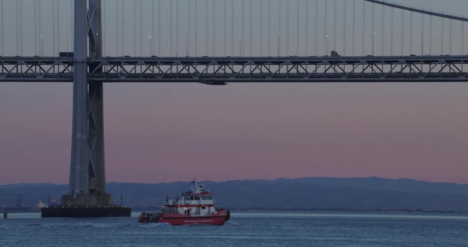 A small boat sailing under a bridge with cars passing by