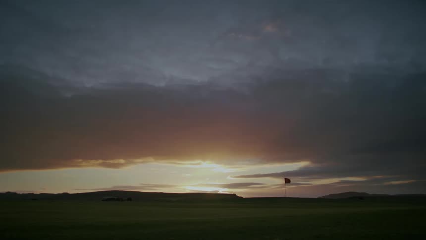 A golf course with a red flag waving against the wind at sunset