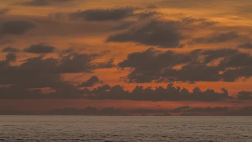 Clouds move over the water as the sun sets in an orange sky