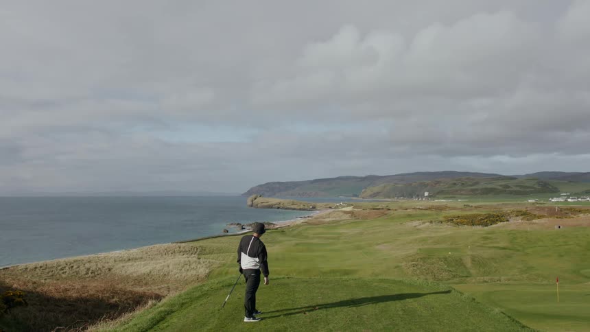 Man playing golf on a peak of a hill on a cloudy day