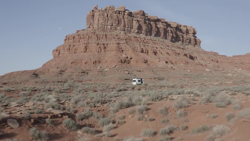 A van is parked off the road among buttes and mesa in the desert