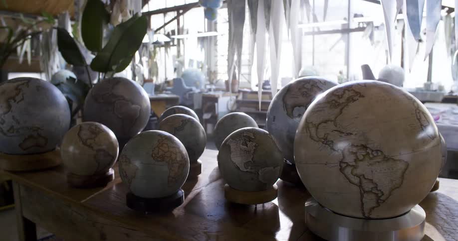 A collection of different globes on top of a desk in front of a bright window in a room that might be a classroom