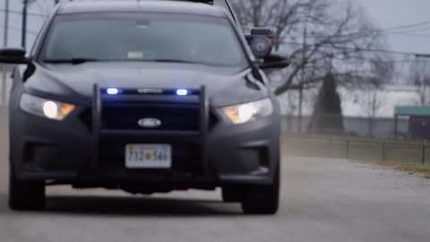 A motorcade of police vehicles pass by with their lights flashing