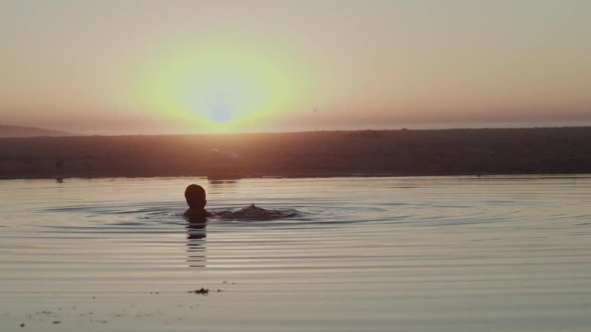 A person is in the water at sunset