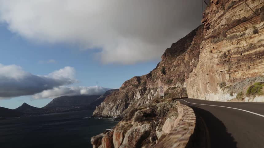 A vehicle drives along a seaside cliff