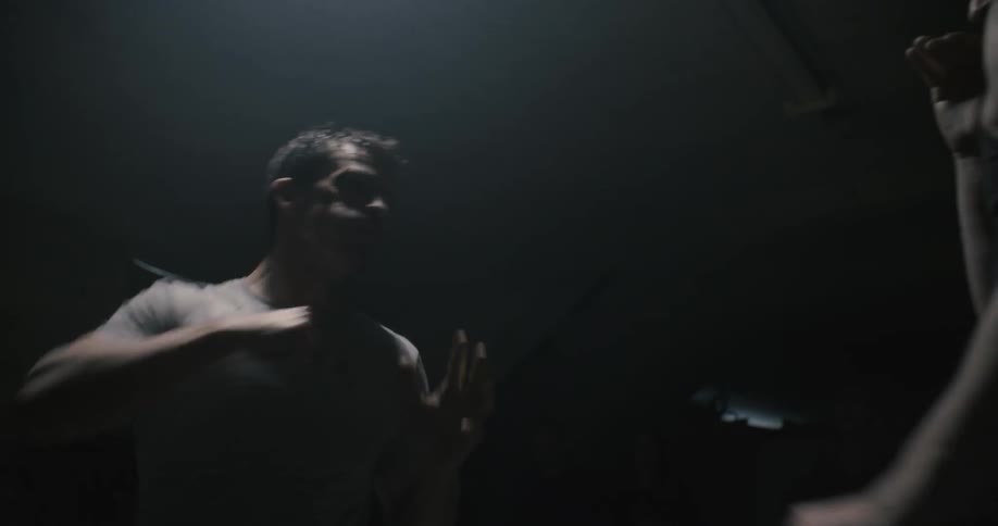 In a darkened room two men fight while others watch