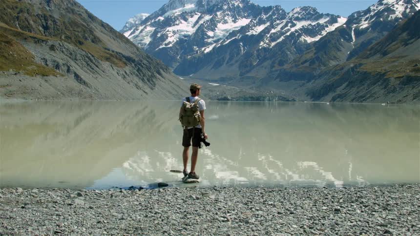 A photographer stands overlooking a mountain lake