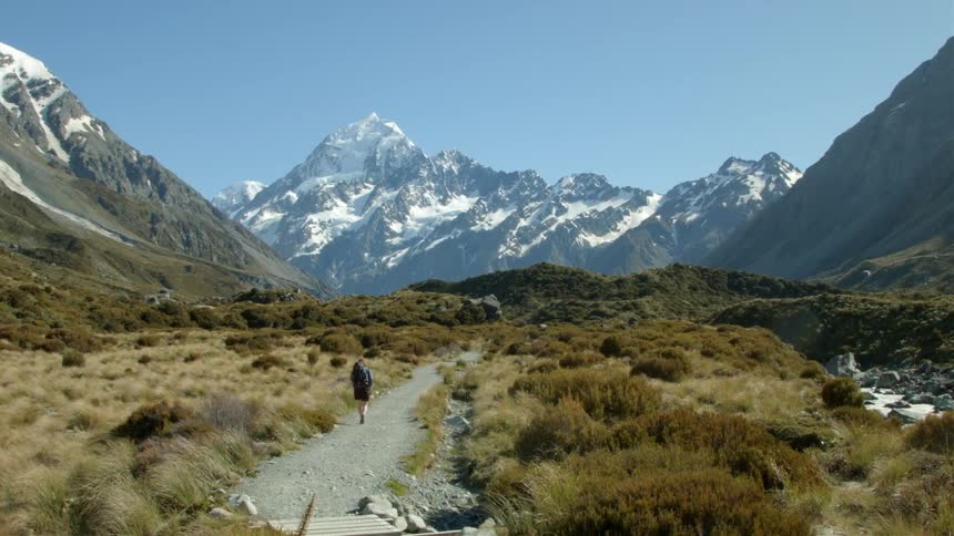 A woman is walking on a trail towards a snow covered mountain